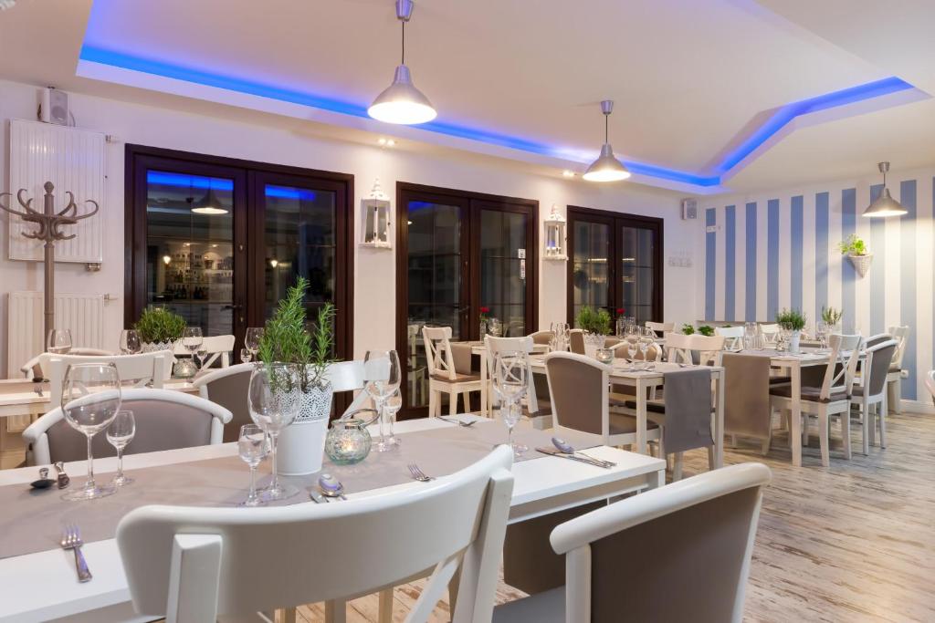 un restaurante con mesas y sillas blancas y ventanas en Villa Puerto, en Pobierowo
