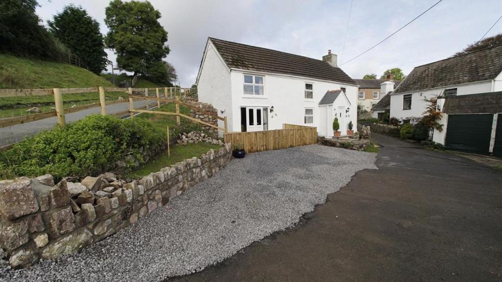 een wit huis met een stenen muur naast een straat bij Frog Lane Cottages in Llanmadoc