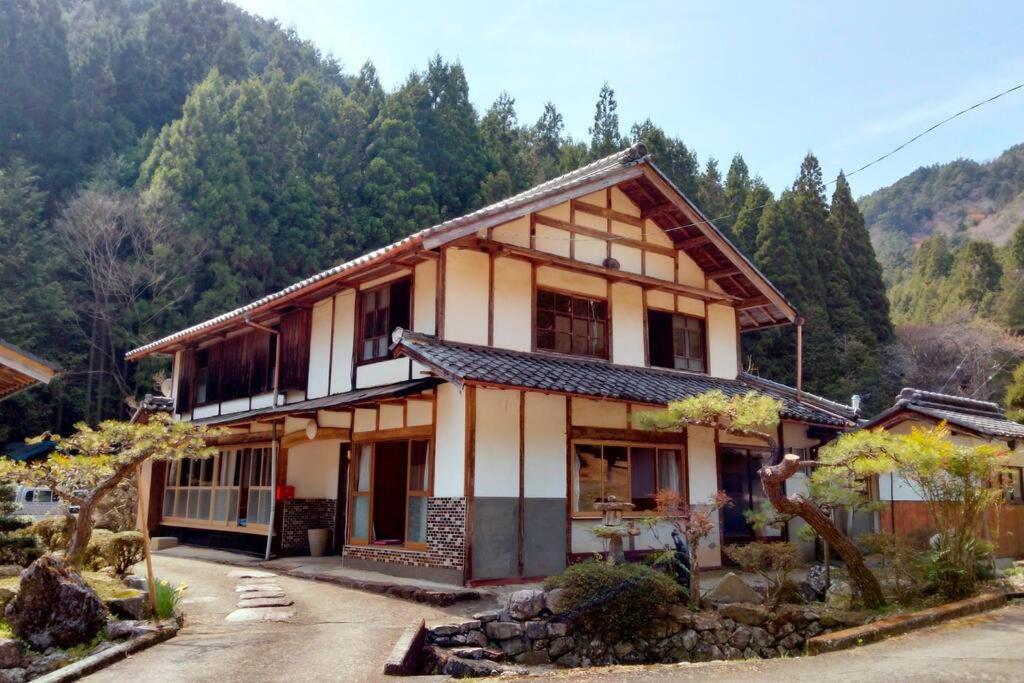 a house with a mountain in the background at 里山アウトドアフィールド・古民家コテージとろせ in Gujo