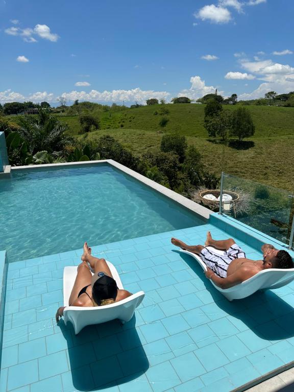 Dos personas tumbadas en sillas en una piscina en Eco Hotel La Colina Mirador en Quimbaya