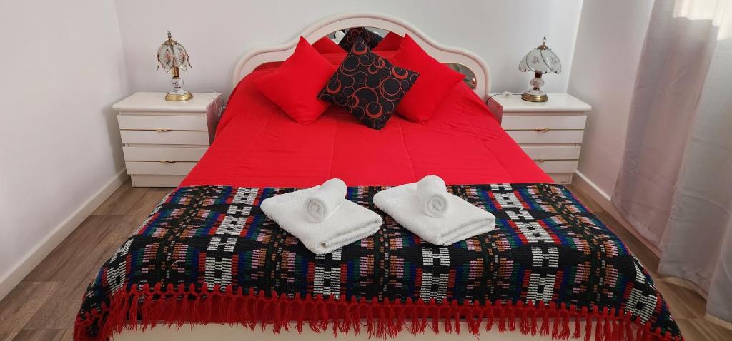 Una cama roja con dos toallas blancas. en Departamento con cochera Mar del Plata en Mar del Plata