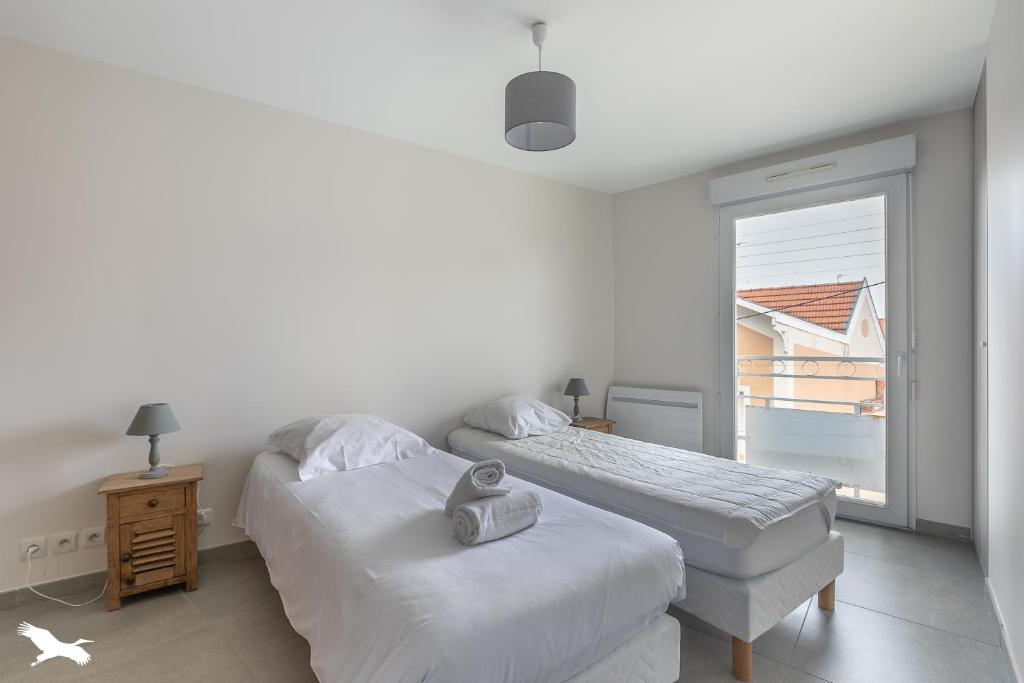 Dos camas en una habitación blanca con ventana. en Villa Rose des sables, en Arcachon