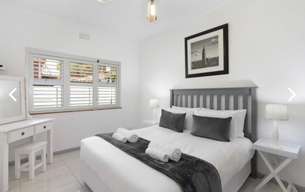 a white bedroom with a bed and a desk at Beautiful Beachfront apartment in Cape Town