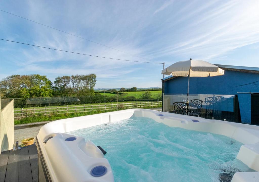 a hot tub on a patio with an umbrella at Gwel y Cambria - Cambrian View in Rhostie