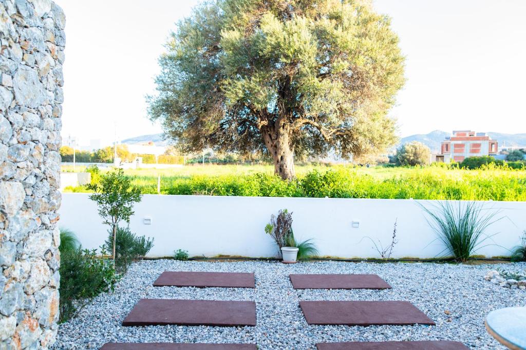 a garden with a tree and a white fence at Pebble Garden Blue Dahlia in Kos