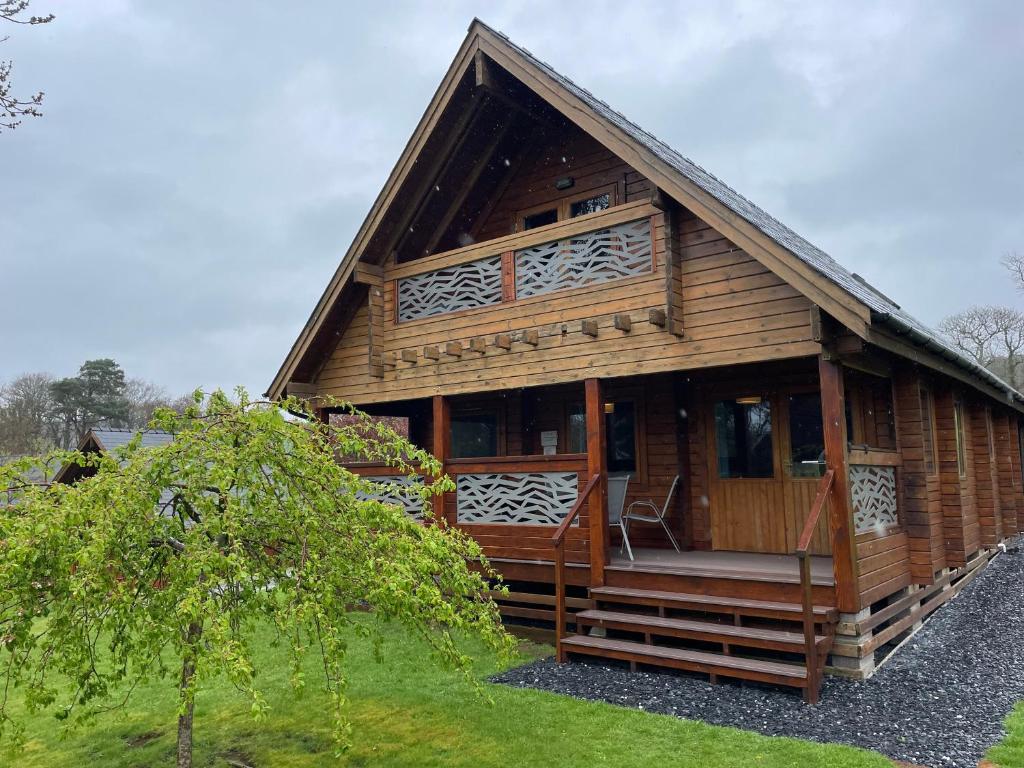 a large wooden cabin with a porch and a tree at Luxury 3 bedroom, 3 bathroom lodge with hot tub in Llanbedr