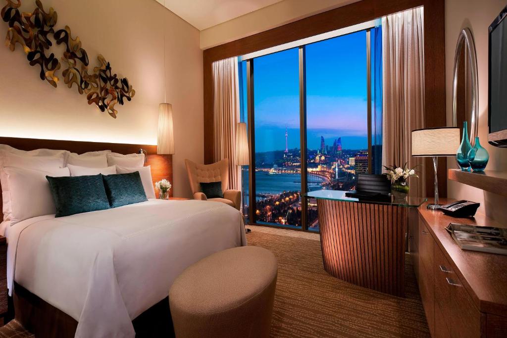 a bedroom with a bed and a desk and a large window at JW Marriott Absheron Baku Hotel in Baku
