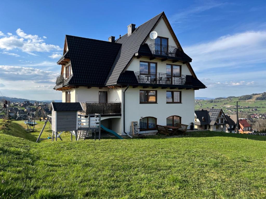 a house with a black roof on a green field at Pokoje u Hani in Bukowina Tatrzańska