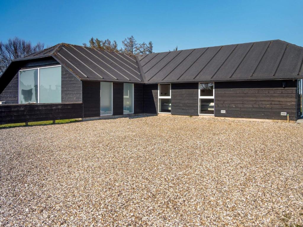 une maison avec un toit noir sur une allée de gravier dans l'établissement Holiday home Snedsted V, à Snedsted