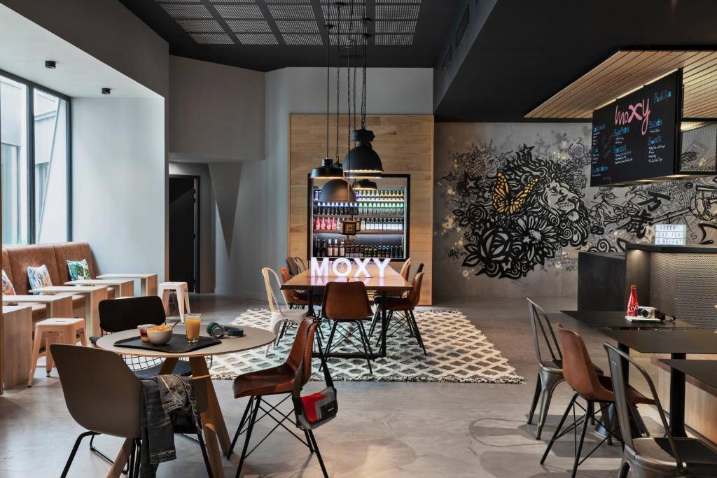 un restaurante con mesas y sillas y una pared con un menú en Moxy Lyon Airport, en Saint-Exupéry
