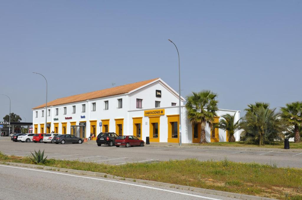 ein weißes Gebäude mit gelben Türen und Autos auf einem Parkplatz in der Unterkunft AS Chucena in Chucena