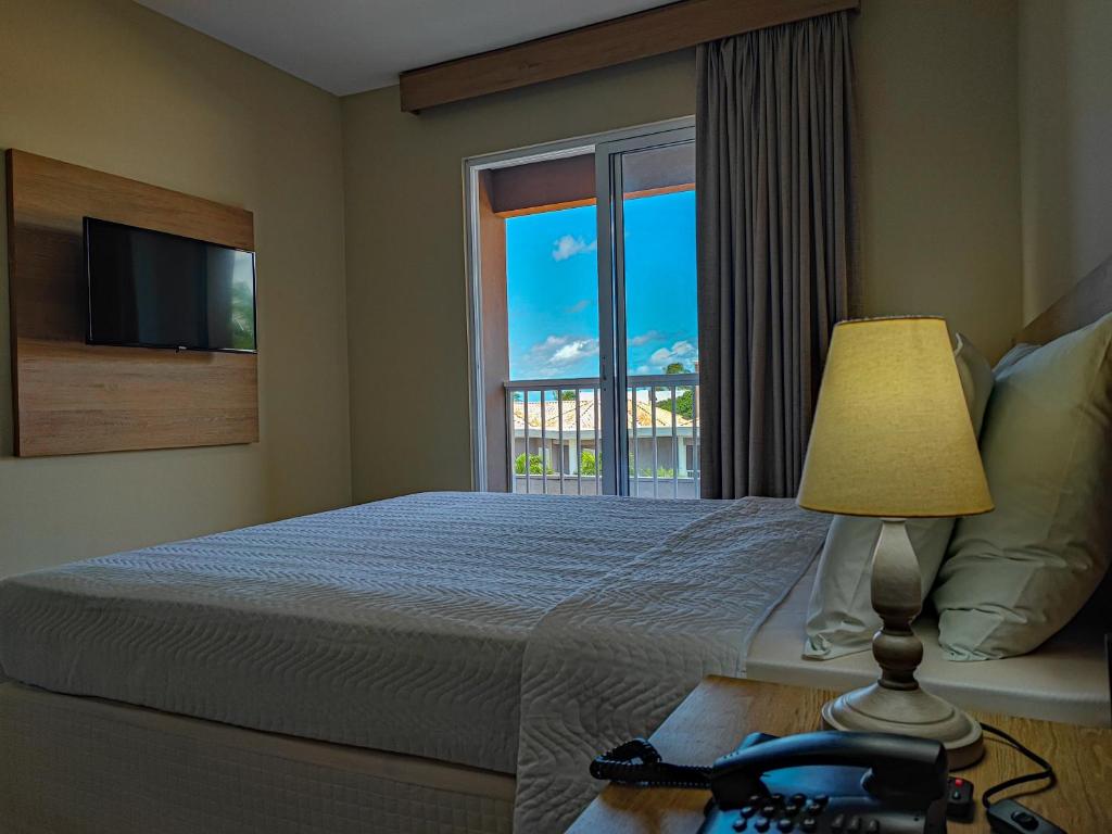 a bedroom with a bed with a window and a lamp at Hotel Coral Beach in Tamandaré