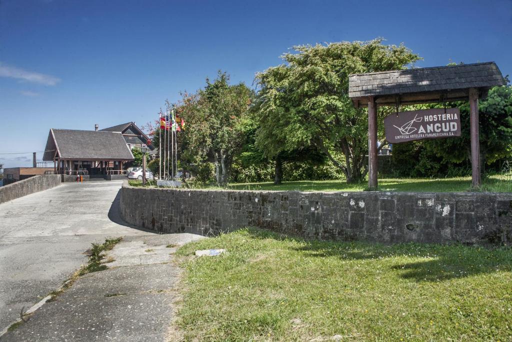 a sign next to a stone wall next to a road at Panamericana Hotel Ancud in Ancud
