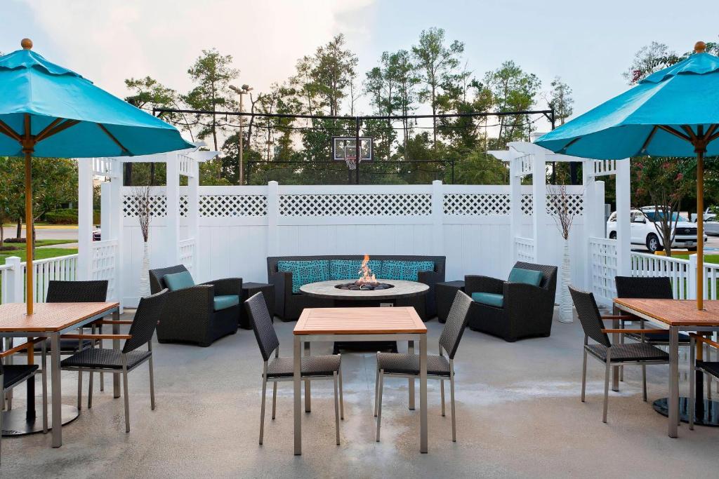 eine Terrasse mit Tischen, Stühlen und blauen Sonnenschirmen in der Unterkunft Residence Inn by Marriott Houston The Woodlands/Lake Front Circle in The Woodlands