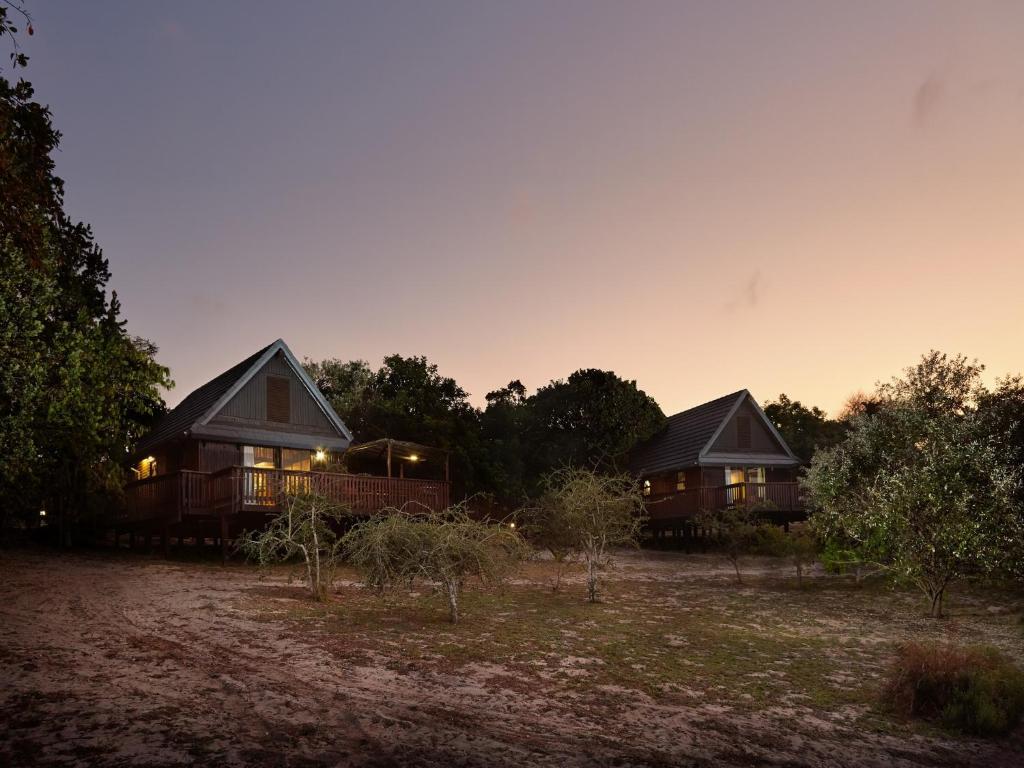 dos cabañas en un campo con la puesta de sol en el fondo en First Group Sodwana Bay Lodge Self Catering en Sodwana Bay