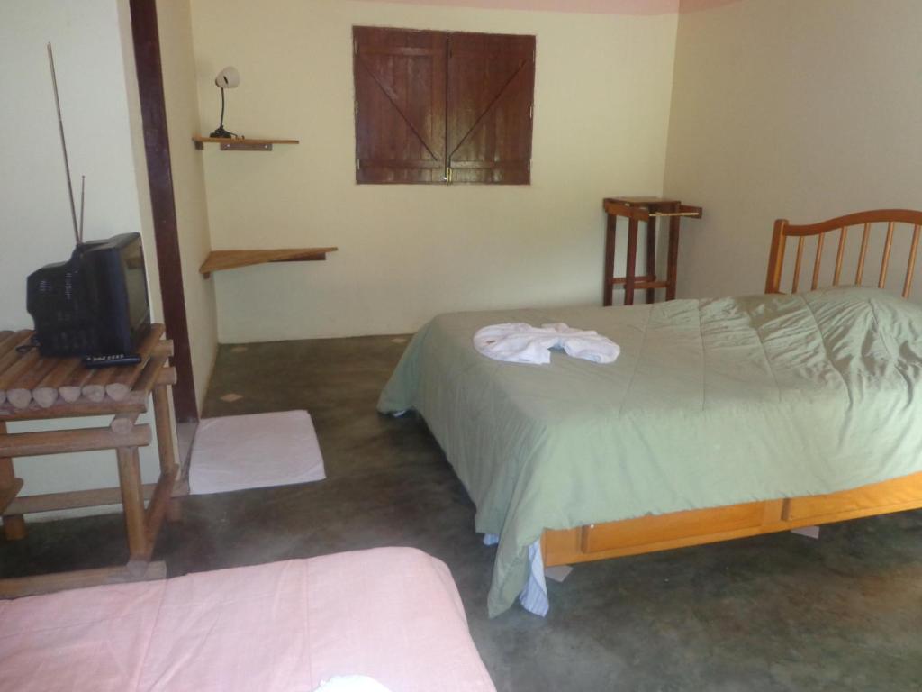 a bedroom with a bed and a tv and a chair at Pousada Chalés do Lago in Cavalcante