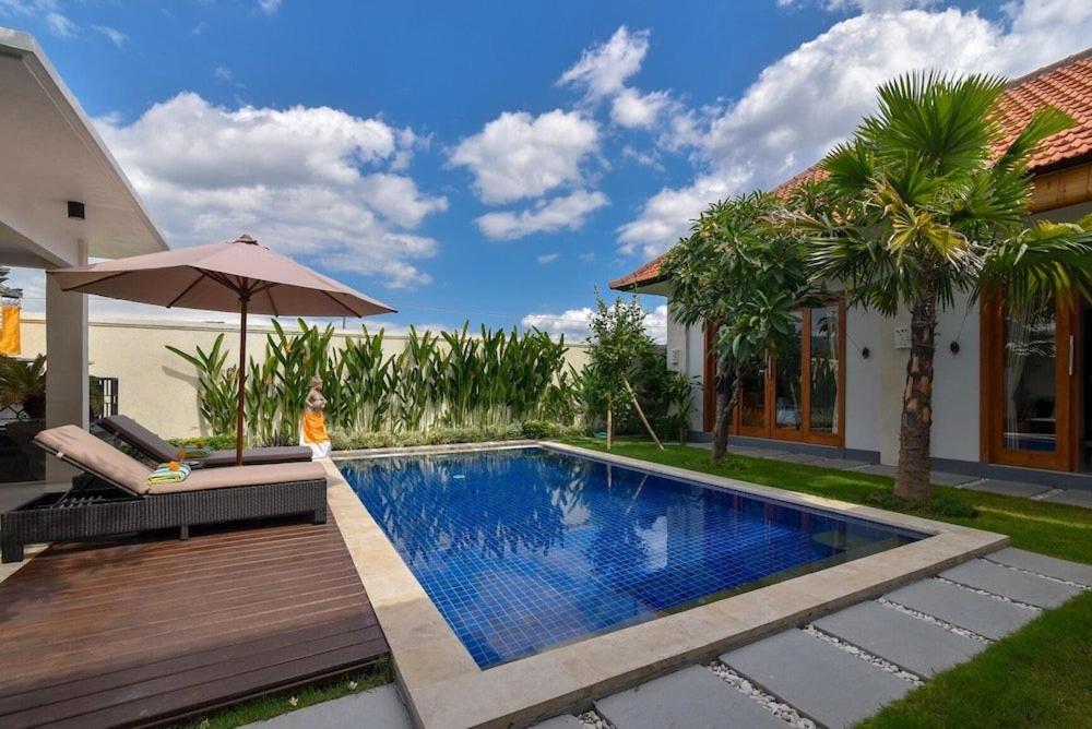 a swimming pool next to a house with an umbrella at Banyu Riris Villa Lovina Private Villa in Banjar