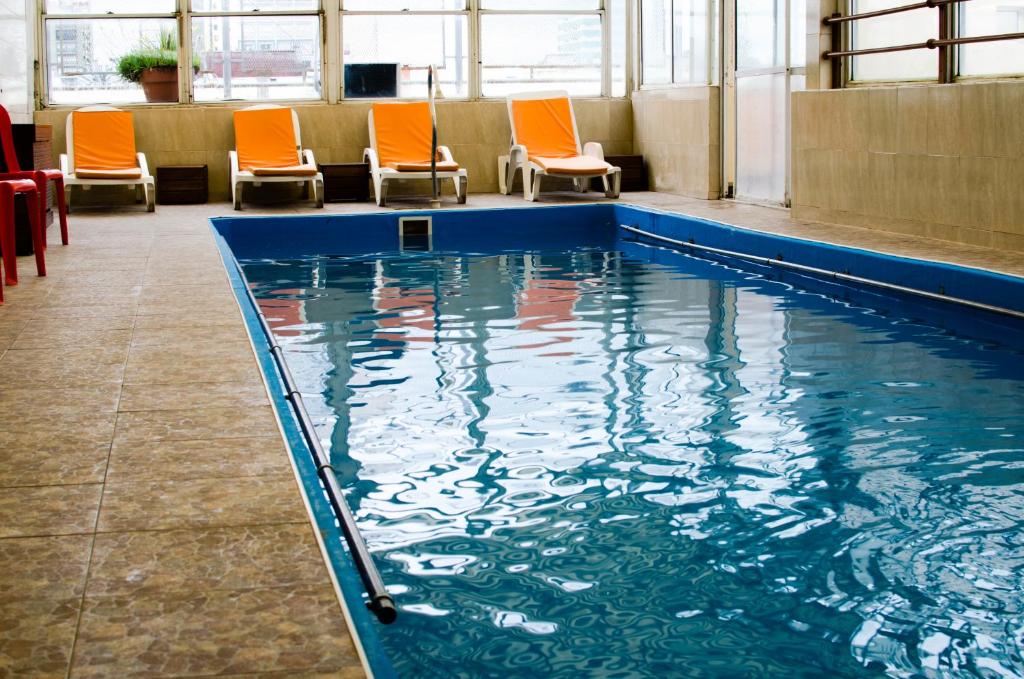 una piscina con sedie arancioni in un edificio di San Remo Grand Hotel a Mar del Plata