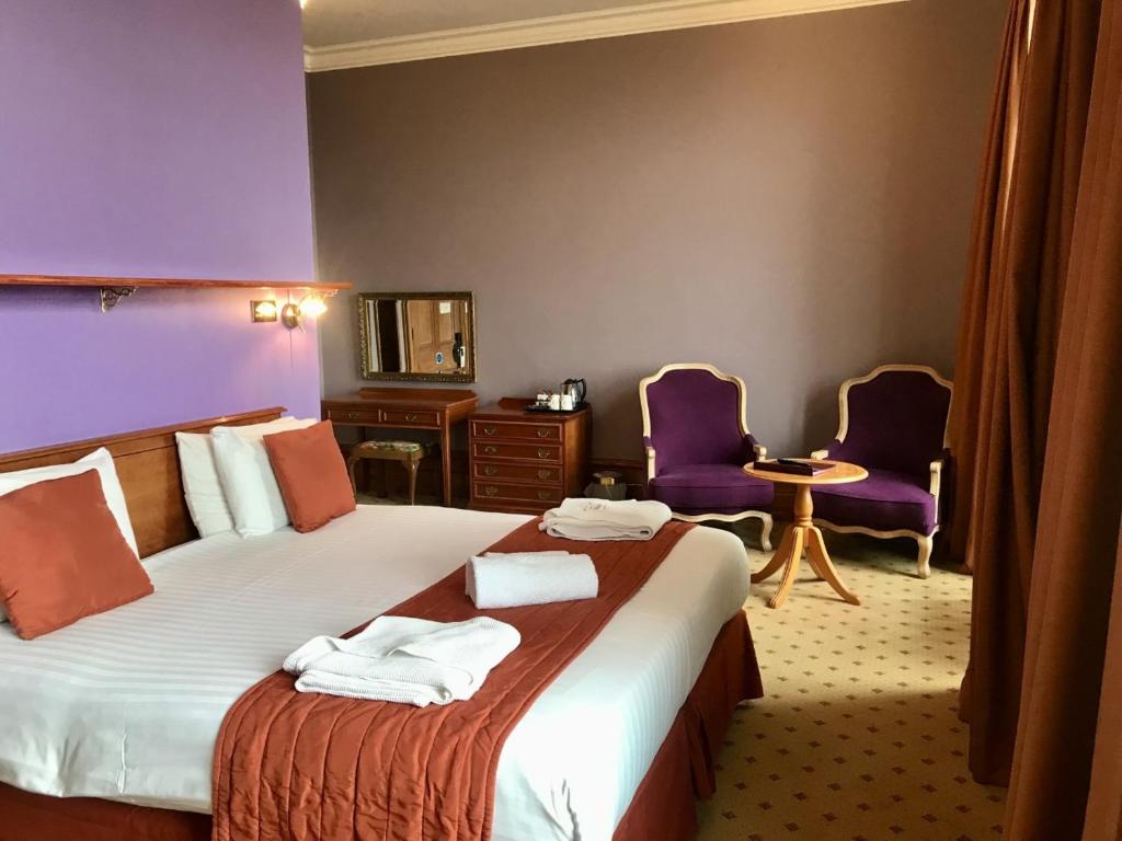a hotel room with a bed and two purple chairs at Purbeck House Hotel & Louisa Lodge in Swanage