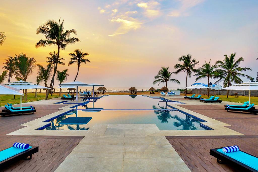een zwembad met stoelen en palmbomen en de oceaan bij Welcomhotel by ITC Hotels, Kences Palm Beach, Mamallapuram in Mahabalipuram