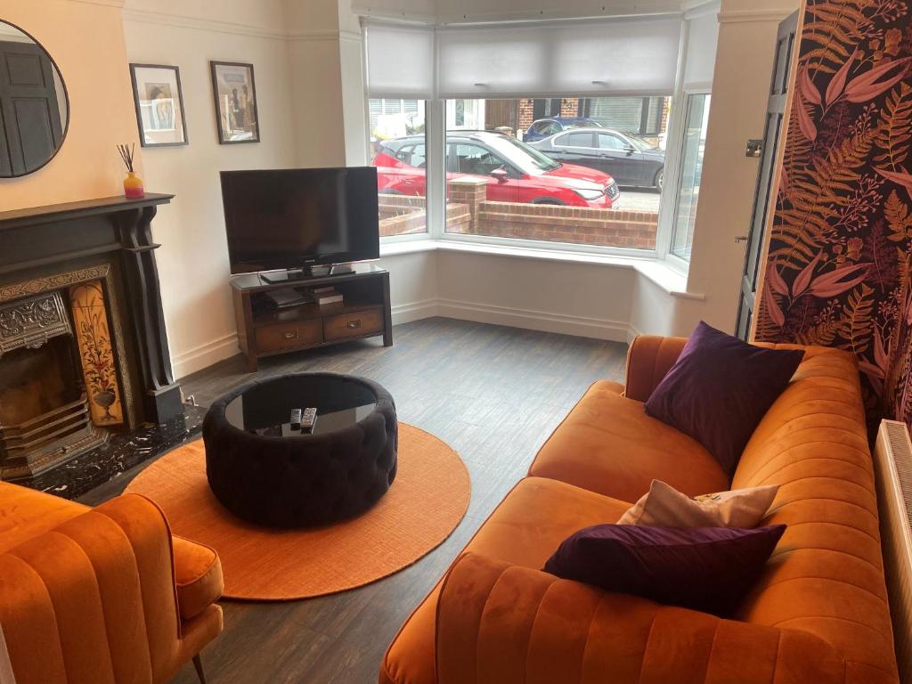 a living room with an orange couch and a tv at Lovely 2 Bed Full House By The Beach in Liverpool