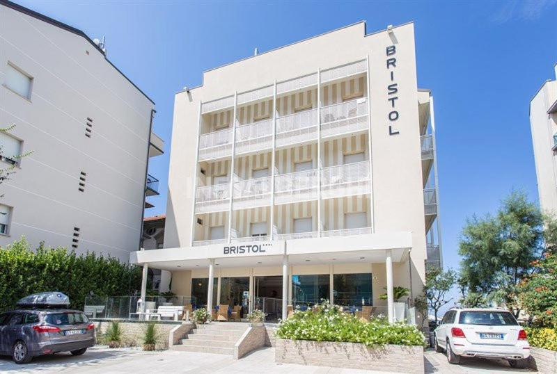 un grand bâtiment blanc avec des voitures garées devant lui dans l'établissement Hotel Bristol, à Cattolica