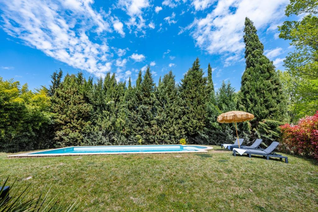 una piscina en un patio con 2 sillas y una sombrilla en La Bastide des Joncquiers, en LʼIsle-sur-la-Sorgue