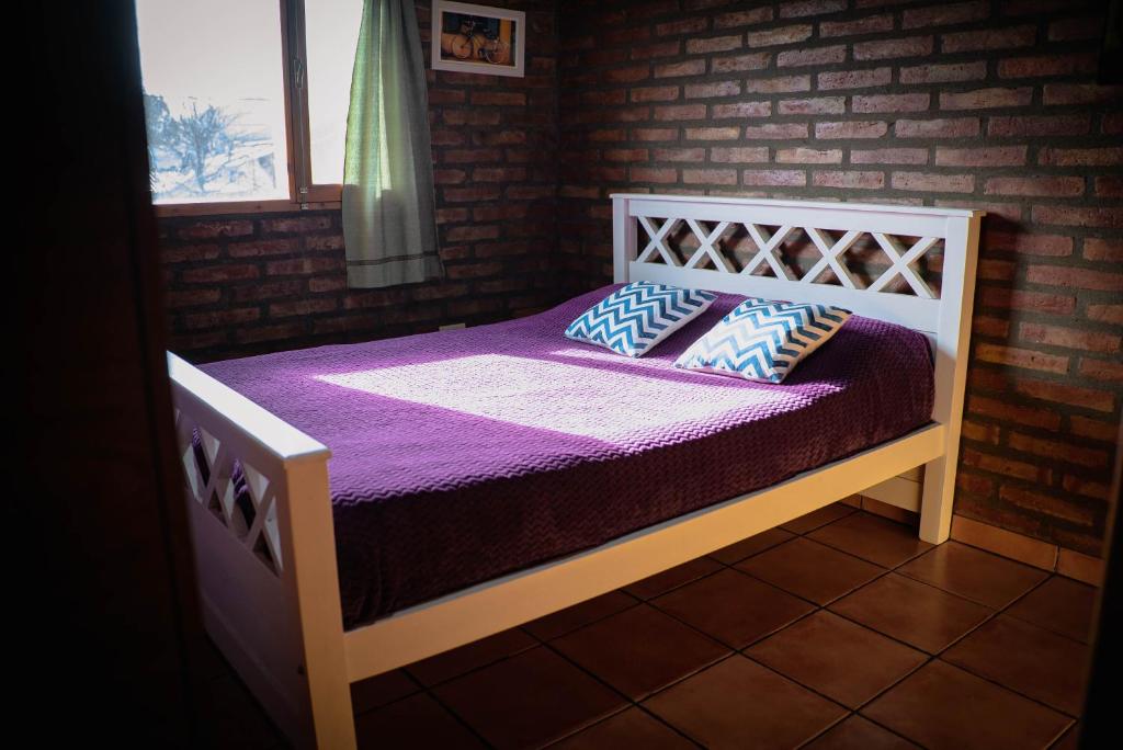 Schlafzimmer mit einem Bett mit lila Bettwäsche und Kissen in der Unterkunft Cabaña Los Lúpulos in El Bolsón