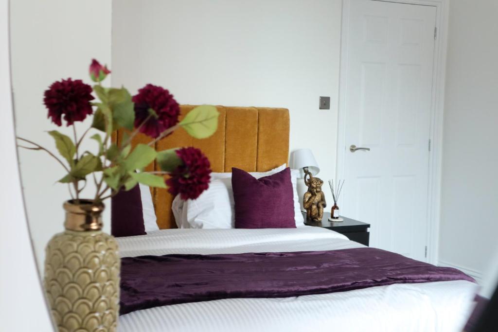 Una cama con almohadas moradas y un jarrón con flores. en Berry's Loft - Central Location and Fast WIFI, en Knaresborough