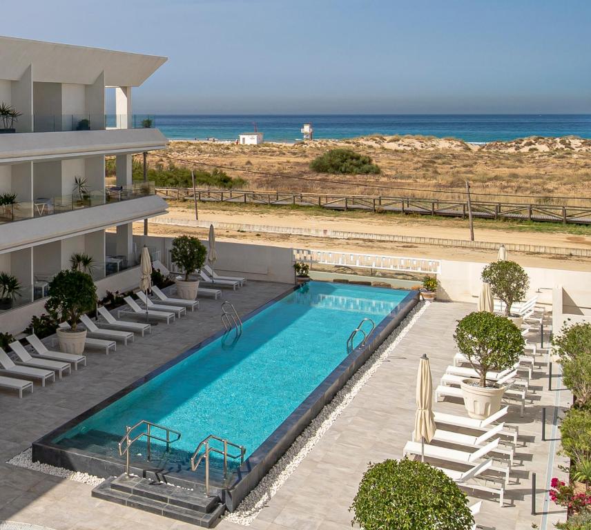 - une piscine avec des chaises et l'océan en arrière-plan dans l'établissement Apartamentos Turísticos Gran Sol, à Zahara de los Atunes