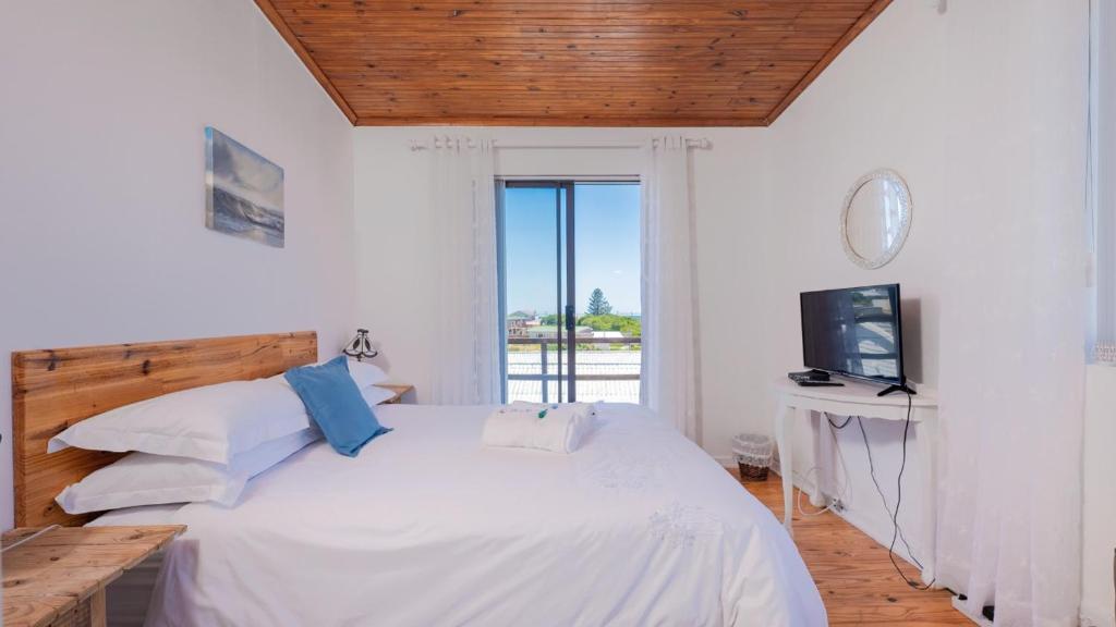 a white bedroom with a bed and a television at Suikerbekkie in Struisbaai