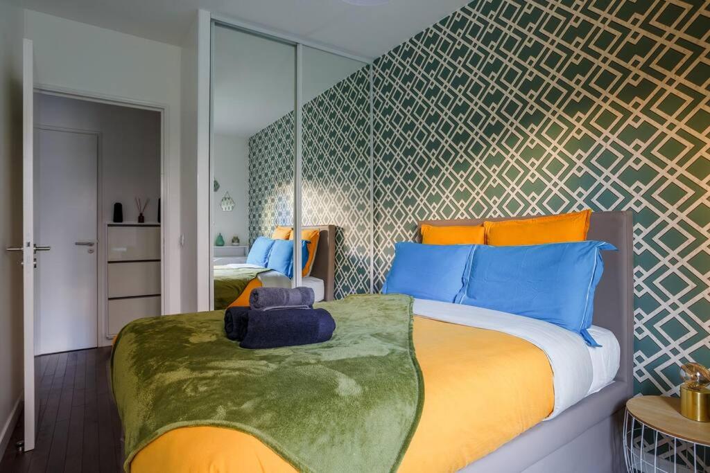 a bedroom with a large bed with blue and orange pillows at Apt 6P - Standing RER Tram Paris Orly Velizy in Le Plessis-Robinson