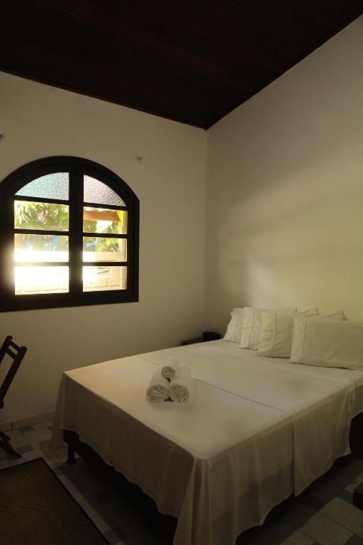 a bedroom with a large white bed with a window at Hospedaria Bem Te Vi Arraial d'Ajuda in Arraial d'Ajuda