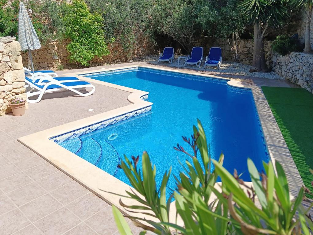 a swimming pool with blue chairs next to a house at Ta’ Peppi Farmhouse in Qala