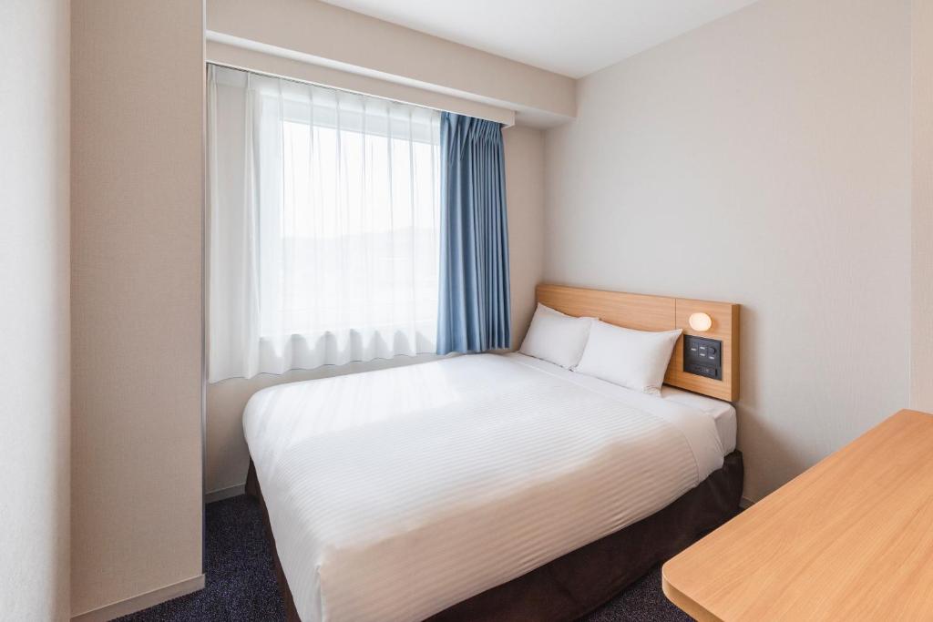 a small bedroom with a bed and a window at Sotetsu Fresa Inn Kamakura-Ofuna kasamaguchi in Kamakura