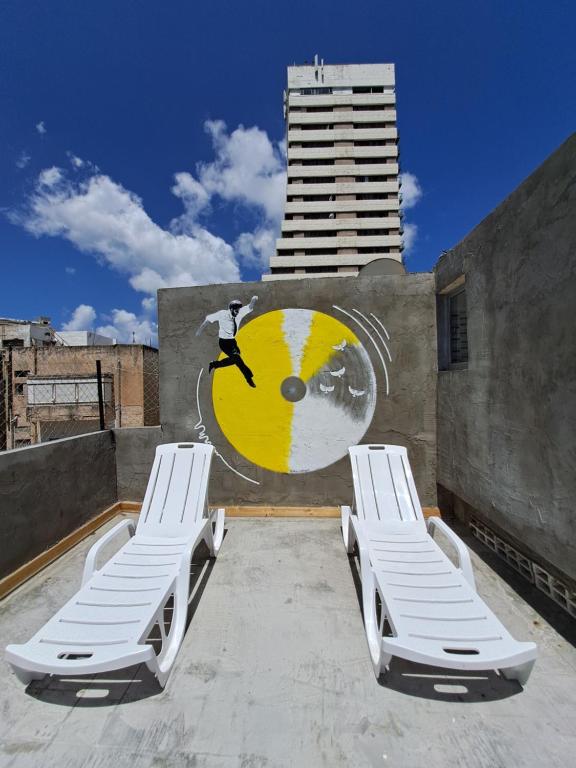 two lounge chairs and a mural on the side of a building at Fellini talpiot roof dolce vita in Haifa