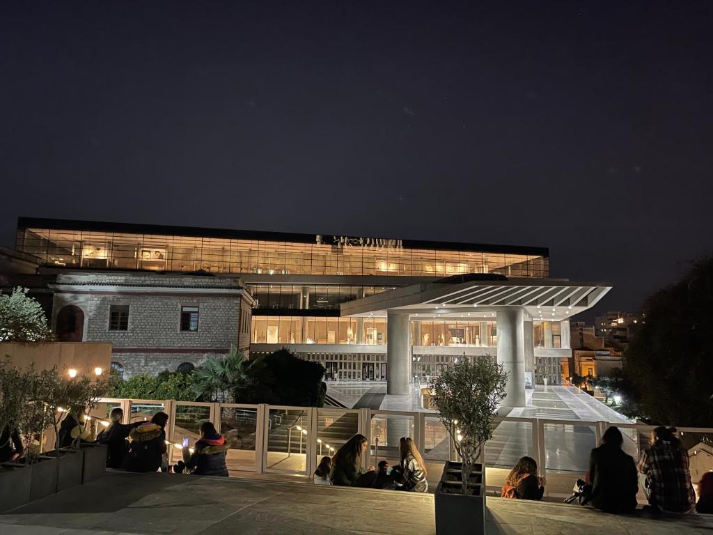 Christina-Anna Athens City Center walking distance to everywhere and Acropolis, in One of the most Favorable Locations by National Gardens and Zoo, Hellenic Parliament in Syntagma and Stylish Exquisite Kolonaki Cozy Renovated Apartment في أثينا: مجموعة من الناس يجلسون خارج المبنى في الليل