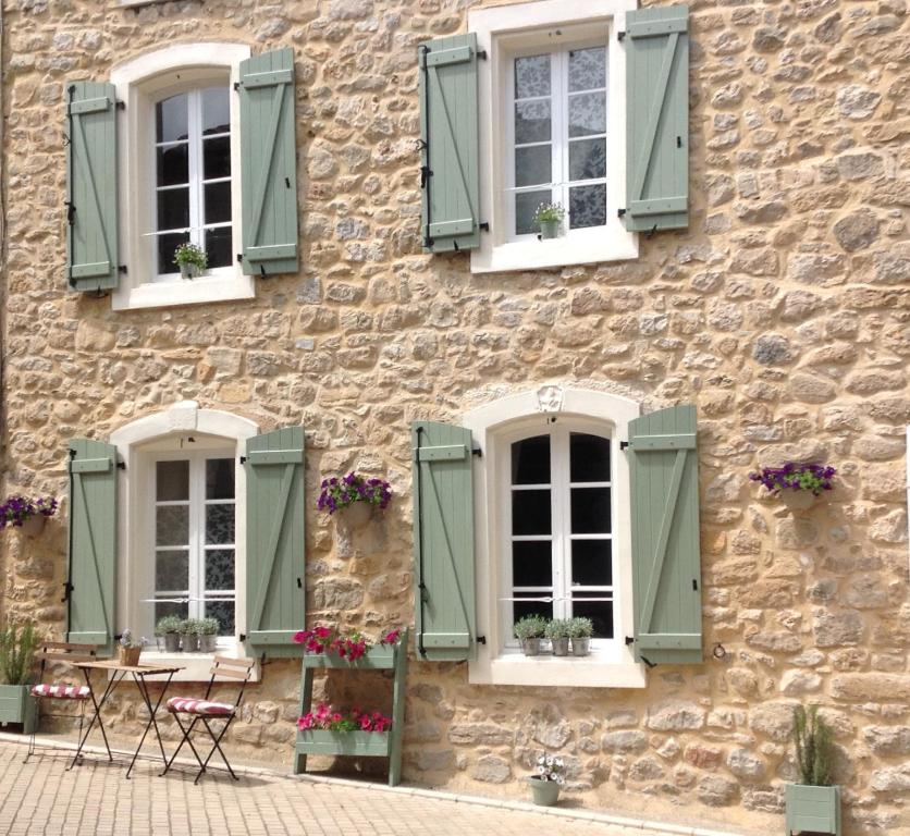 a stone building with green shutters and a table and chairs at Maison de L'Amour Apartment Chardonnay in Assignan