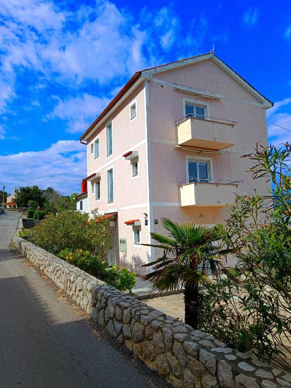 a pink building with a stone wall next to a street at Studio Apartmani Zorić in Šilo