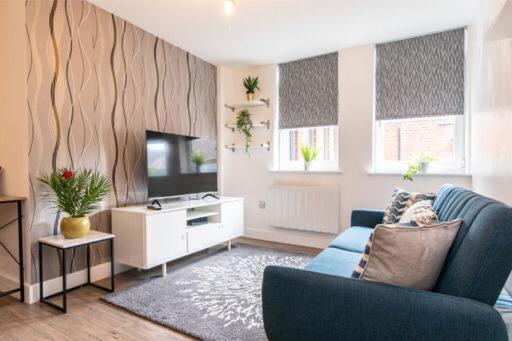 a living room with a blue couch and a tv at Queens House Apartment in Coventry