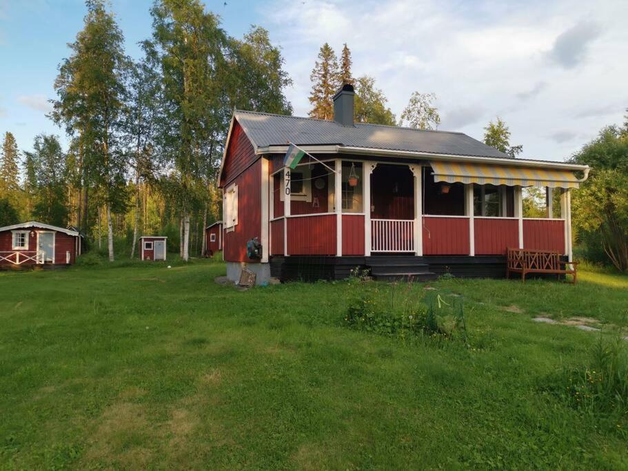 una casa roja con un porche en un campo de hierba en Cabin 70m from lake. Big garden, en Östersund