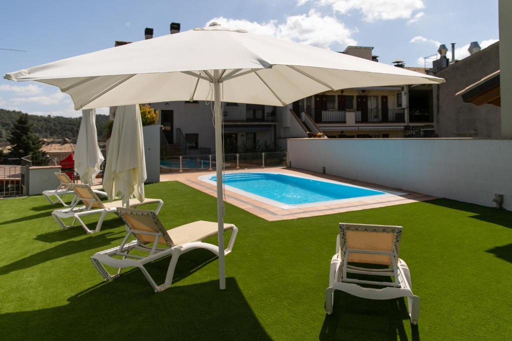 un patio con sillas, una sombrilla y una piscina en Aparthotel Cal Marçal en Puig-reig