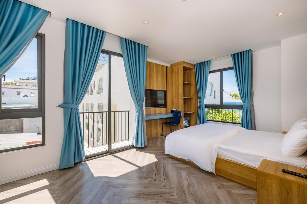 a bedroom with blue curtains and a bed with a large window at Cát Lợi Phú Quốc Hotel in Phu Quoc