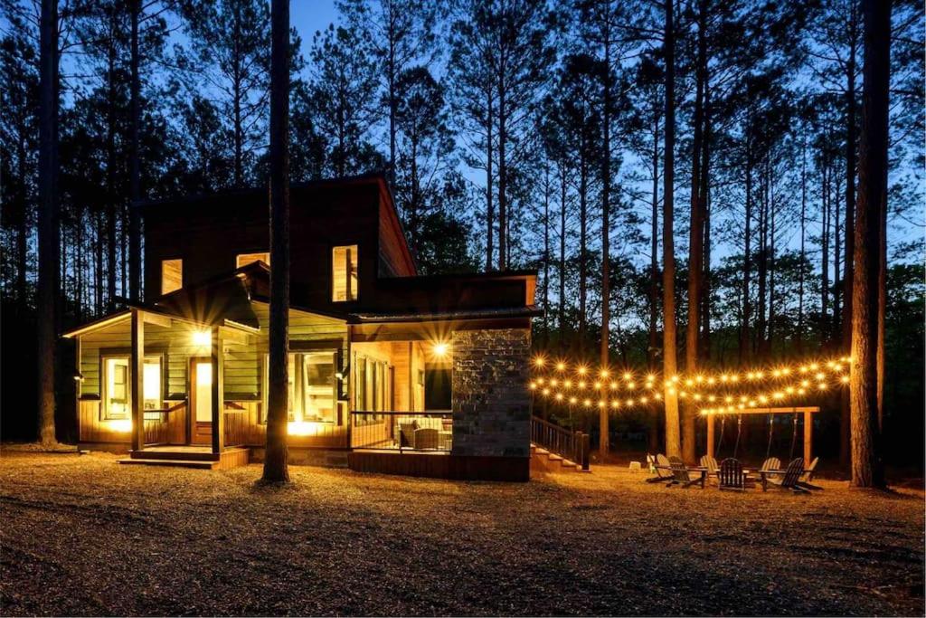 a house with christmas lights in the woods at night at Brand New Luxury 2 Bedroom with Loft and Spa Sleeps 10 in Broken Bow