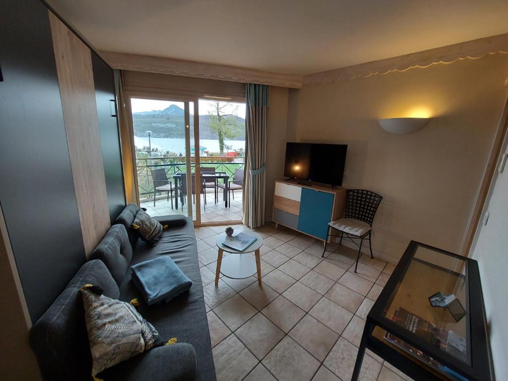 a living room with a couch and a television and a table at Logement avec terrasse sur lac, tout confort, dans résidence avec PLAGE et PONTON PRIVEE in Duingt