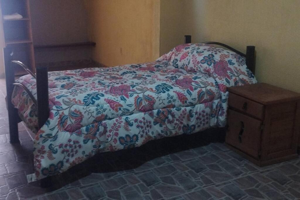 a bed with a flowered comforter and a wooden table at Casa en Joyas Cuautitlan grande y cómoda in Cuautitlán