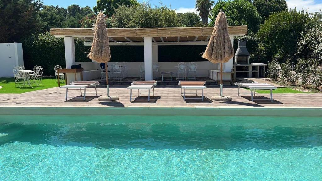 a swimming pool with two umbrellas and chairs and a patio at Oltre la Vite in Selva di Fasano