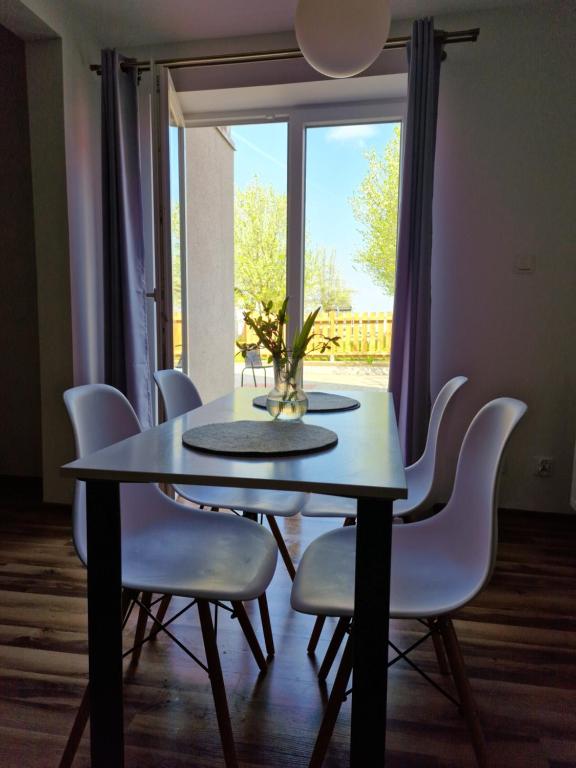 a dining room table with white chairs and a window at Apartamenty Mikołajki na Kajki in Mikołajki