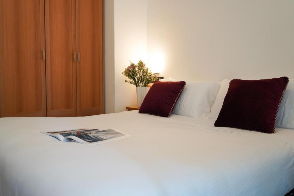 ein weißes Bett mit roten Kissen und eine Zeitschrift darauf in der Unterkunft Hotel Sunset in Rimini