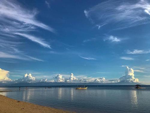 a beach with a boat in the water and a cloudy sky at Casa Astillero - Calatagan Batangas Private Resort in Calatagan
